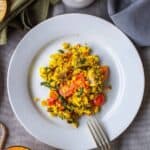 Tofu revuelto vegano con espinacas y tomates cherry servido en plato blanco con pan y bebida al lado.