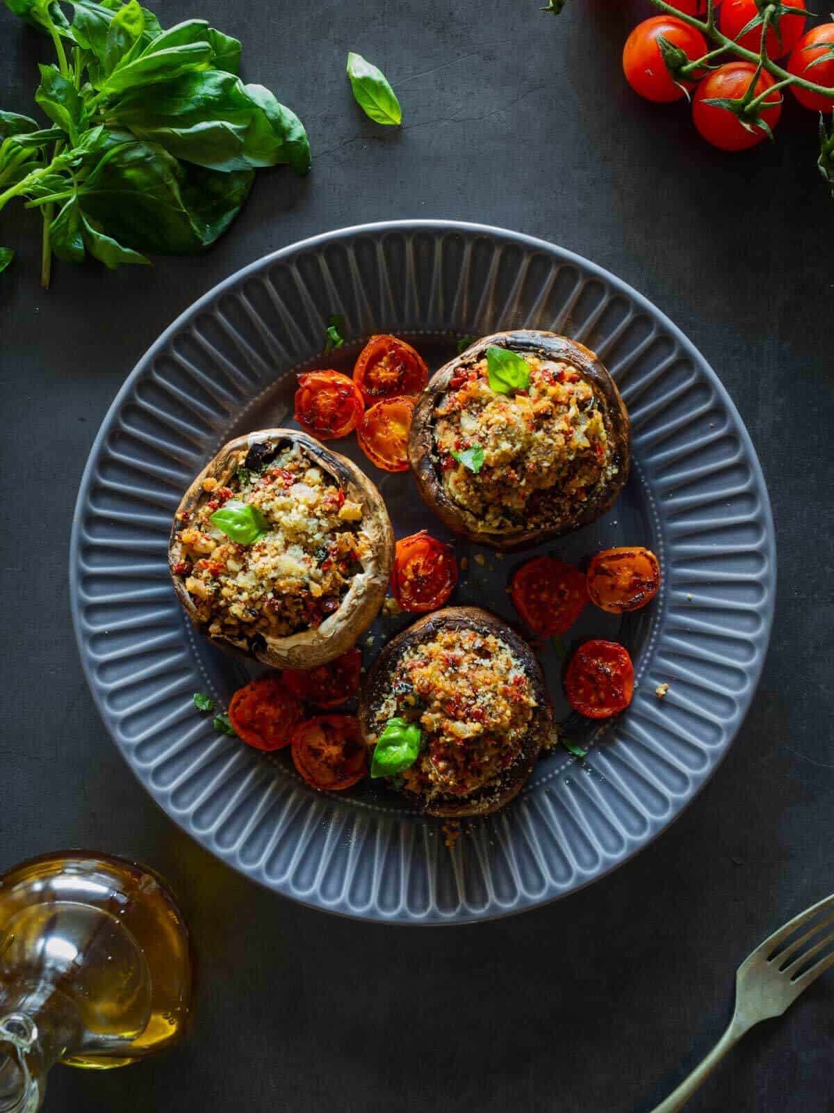 Champiñones portobello rellenos sobre un plato azul, con un enfoque en los tomates cherry como guarnición.