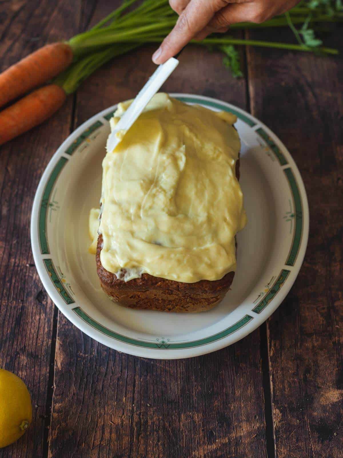 untando glaseado sobre la tarta de zanahoria con una espátula.
