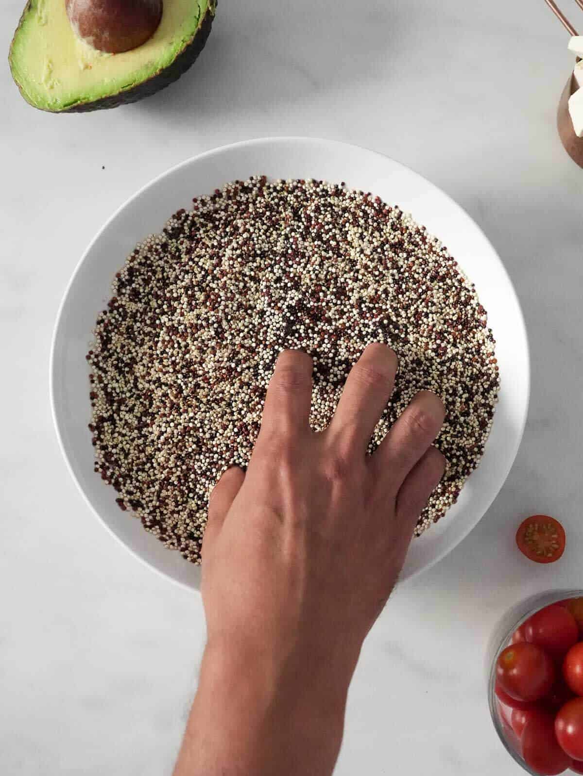 remojando quinoa y revolviendolo con la mano en un bowl blanco.