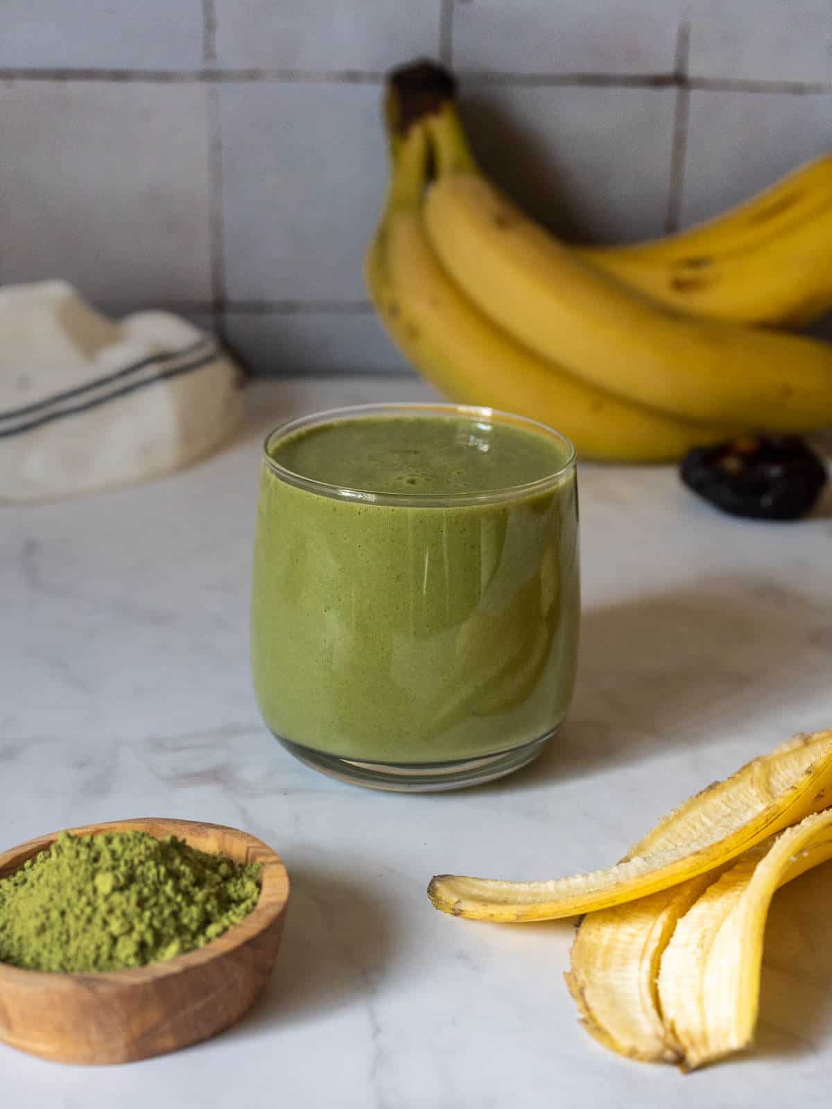 un vaso de batido de té verde matcha y banana con una cazuela de té verde matcha en polvo.