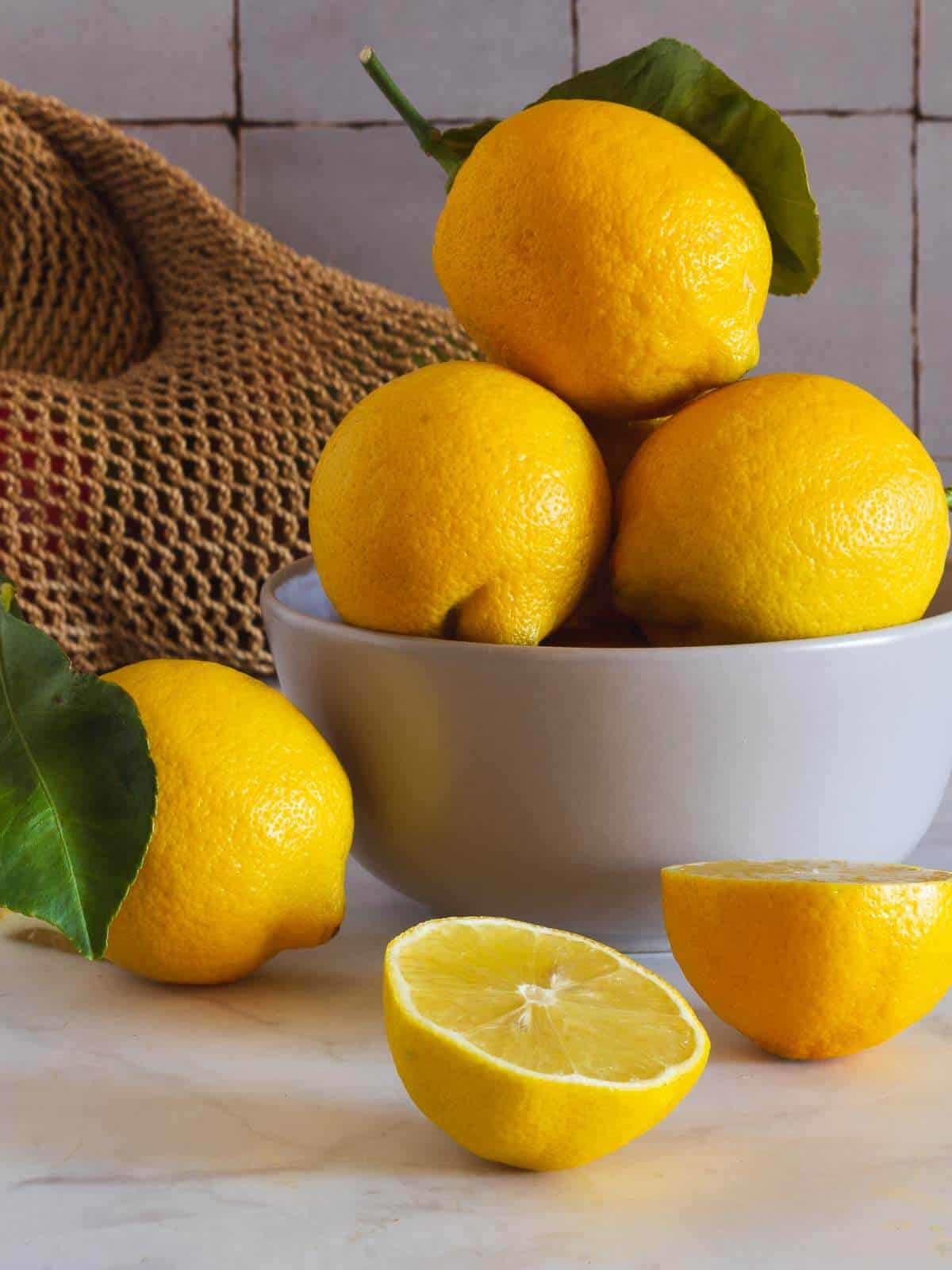 bowl blanco con limones y dos mitades sobre mesa blanca.
