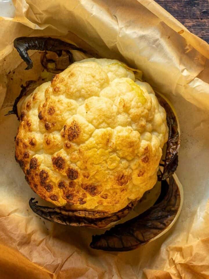 cabeza de coliflor rostizada al horno entera sobre fuente cubierta de papel pergamino.