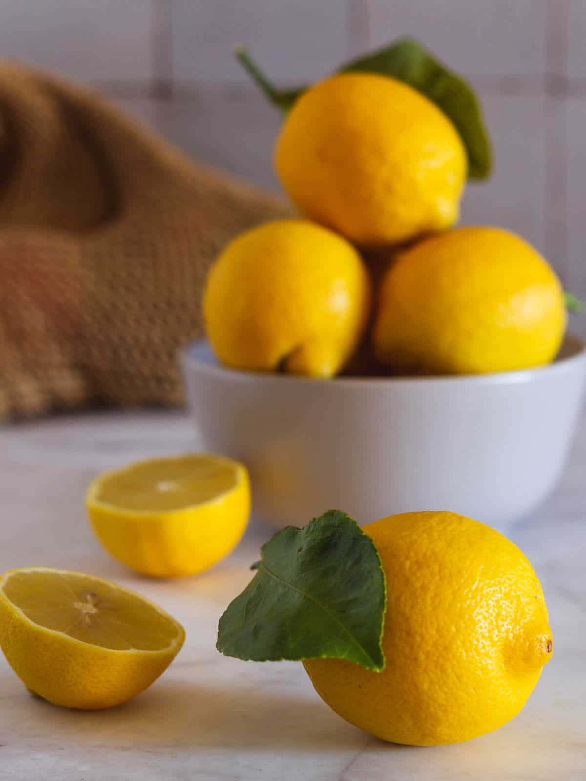 bowl con limones enteros y dos sobre la mesa.