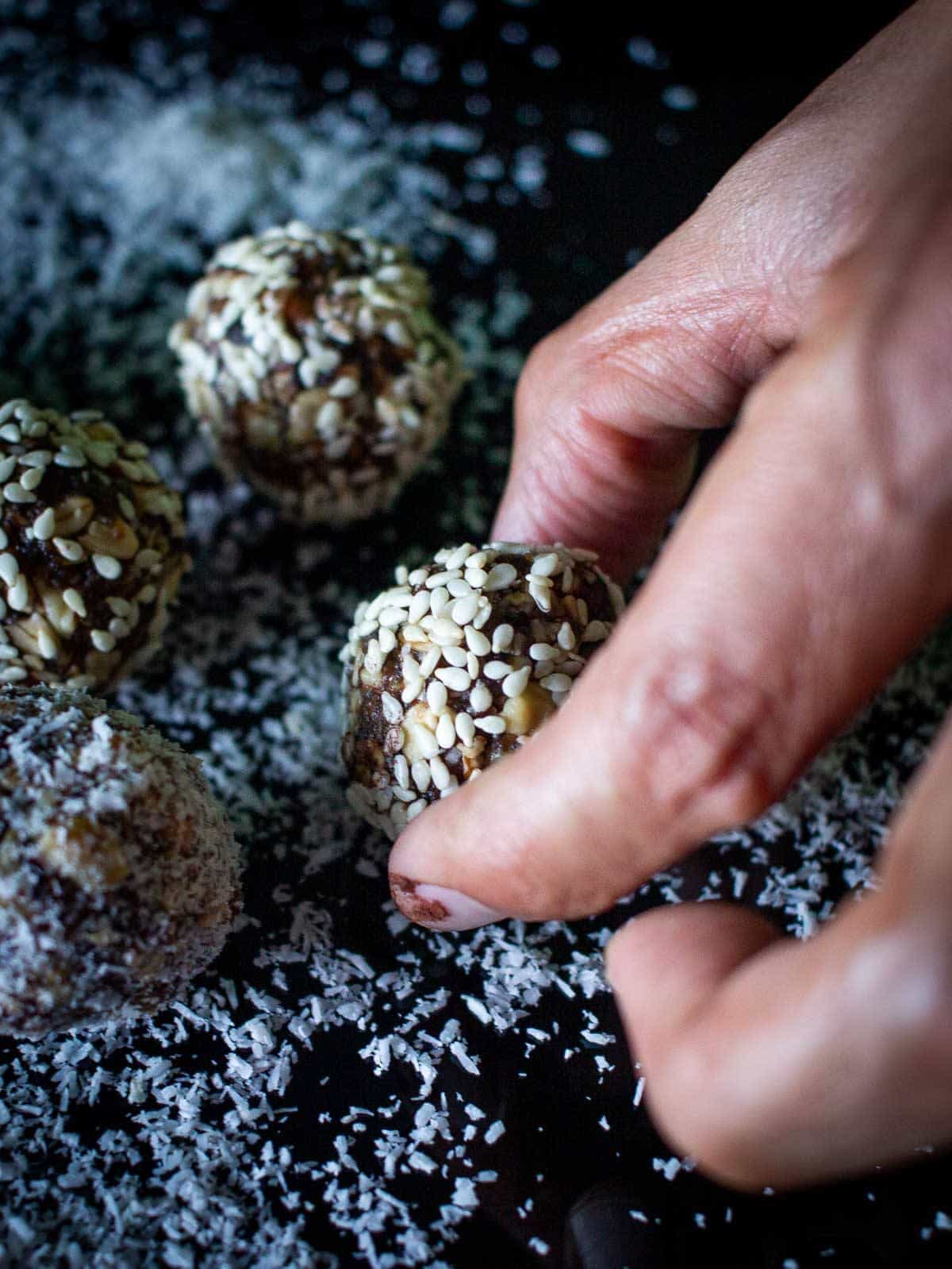 mano acomodando trufas de chocolate sobre coco rallado.