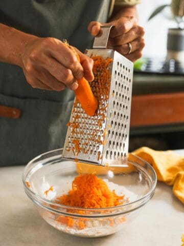 rallar las zanahorias en un rallador de caja sobre los ingredientes húmedos.