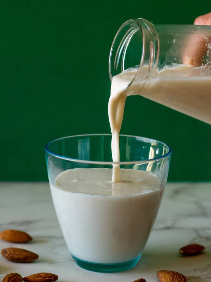 botella sirviendo leche de almendras casera en un vaso.