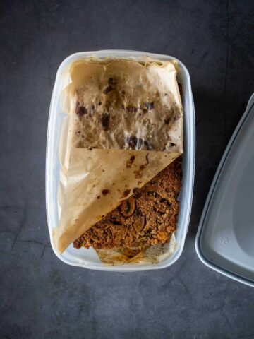 pastel de carne vegano guardado en un recipiente hermético con papel pergamino en la parte superior e inferior.