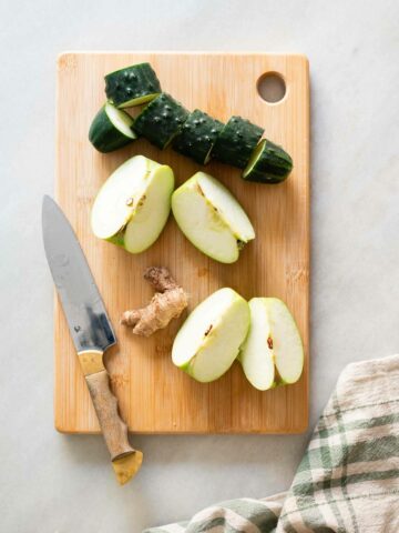 jengibre, pepino y manzana verde cortados sobre tabla de madera.