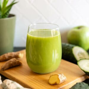 un vaso con jugo verde detox junto a sus ingredientes frescos.