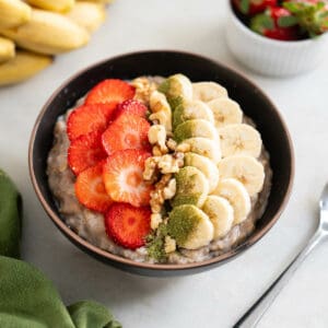 receta proteica de avena servida en un bowl, decorada con rodajas de frutilla y banana frescas.