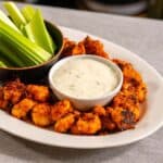 alitas de coliflor búfalo crujientes servidas con dip ranch vegano y bastones de apio, un aperitivo saludable y delicioso.