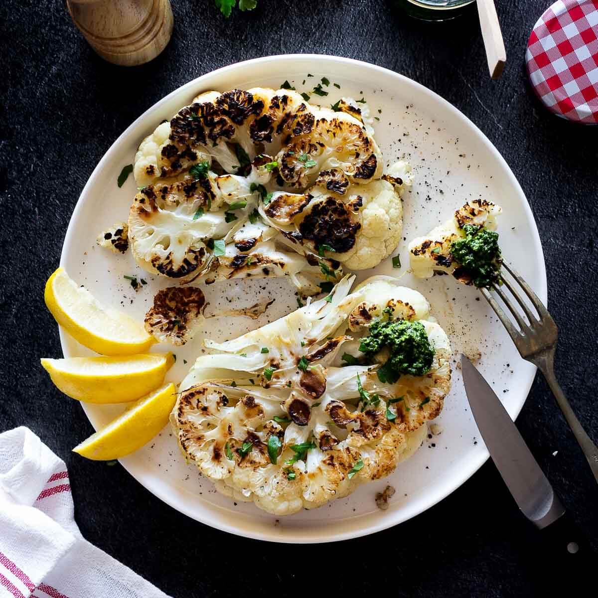 coliflor a la plancha servida con rodajas de limón y pesto.