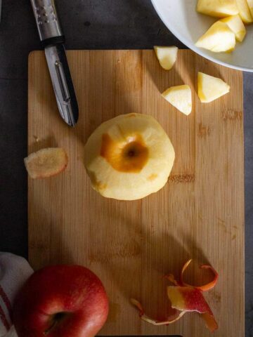 una manzana pelada y otra roja sin pelar sobre tabla de cortar.