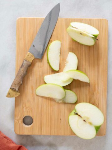 manzana verde cortada en rodajas finas sobre una tabla de cortar.