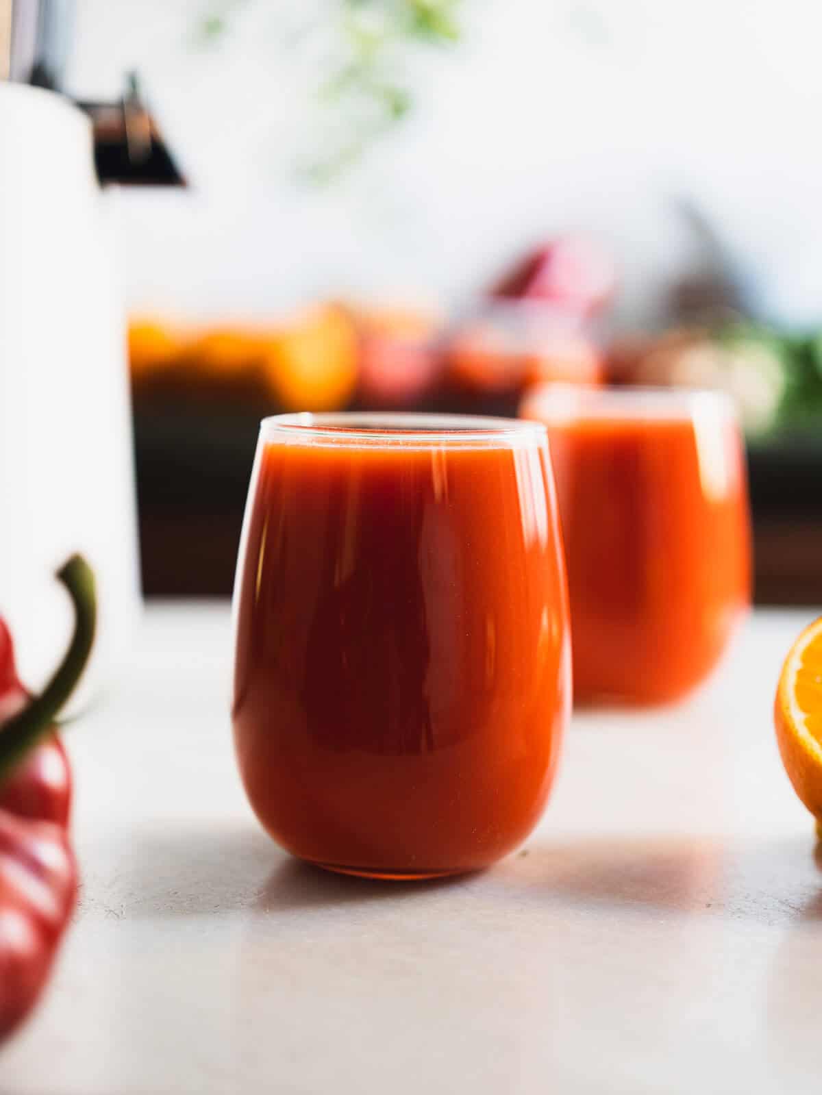 dos vasos sobre la mesa servidos con jugo de pimiento rojo y zanahoria.