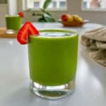 licuado de espinacas para adelgazar en un vaso con una rodaja de frutilla sobre la mesa.