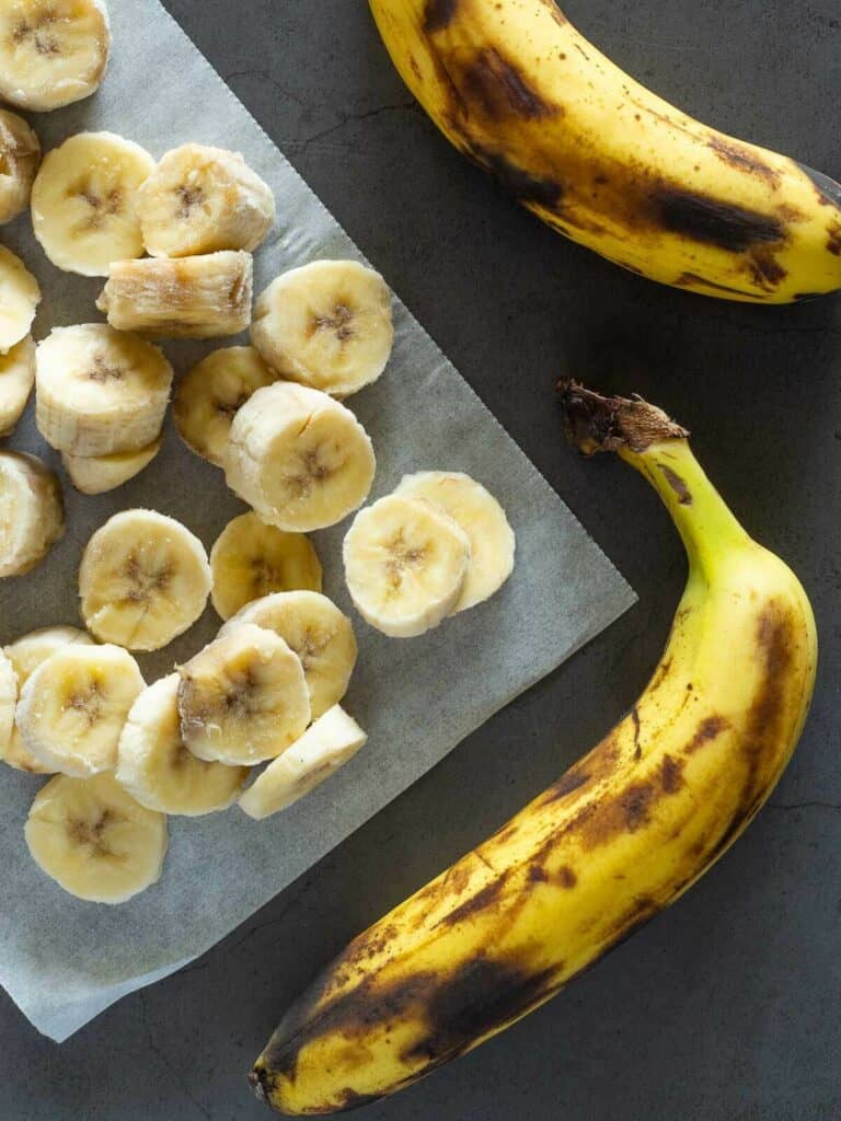 rodajas de plátanos congelados, junto a dos enteros sin pelar.