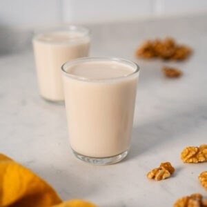 leche de nueces en un vaso junto a nueces en mitades sobre la mesa.