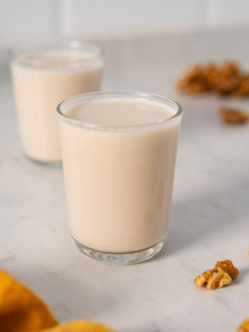 leche de nueces en un vaso junto a nueces en mitades sobre la mesa.