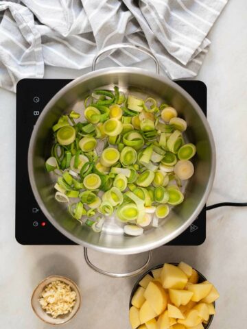 puerros en rodajas rehogándose en una olla, con ajo picado y patatas listas para el siguiente paso de la receta de sopa de puerros y patatas.