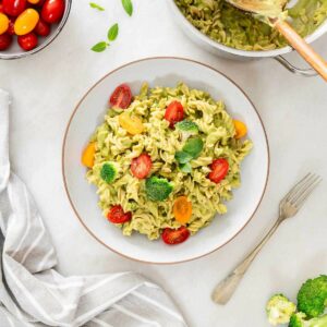 tazón de pasta con brócoli cremosa con guarnición de tomates cherry cortados por la mitad, brócoli y hojas de albahaca fresca.