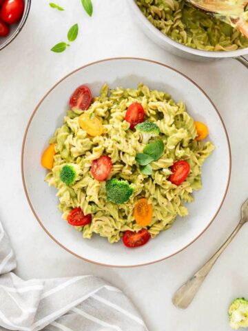 tazón de pasta con brócoli cremosa con guarnición de tomates cherry cortados por la mitad, brócoli y hojas de albahaca fresca.