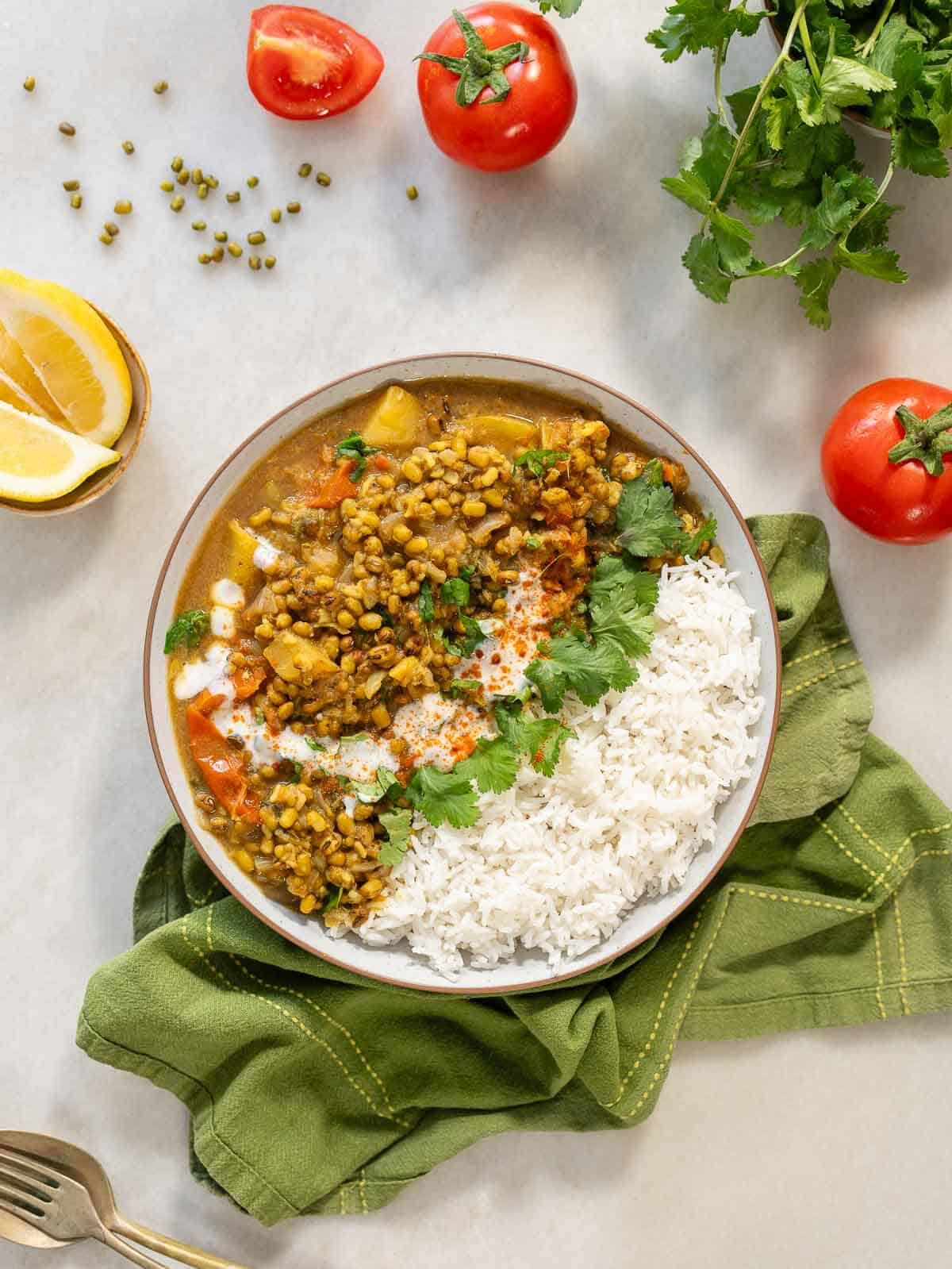 sopa de judía mungo servida junto a arroz basmati en el mismo bowl, junto a tomates.y limón sobre la mesa.