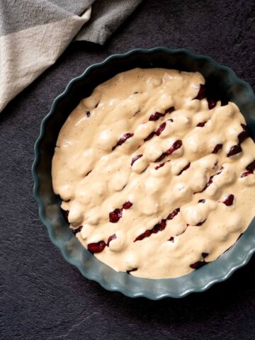 Molde para tarta con la masa vertida sobre las cerezas.