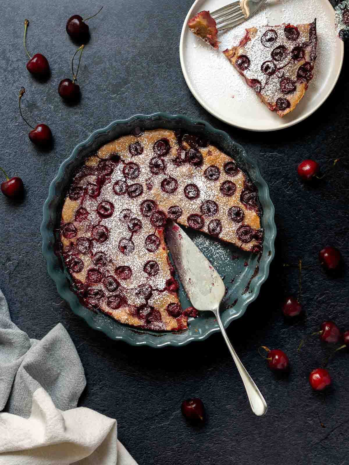 Tarta de cerezas horneada con una porción cortada y una espátula para servir.