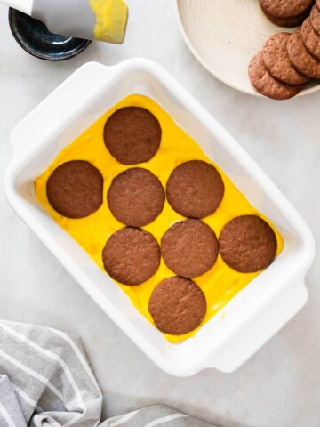 Vista superior de una tarta galletas de chocolate y crema de calabaza en una fuente rectangular, con la primera capa de calabaza y galletas de chocolate.