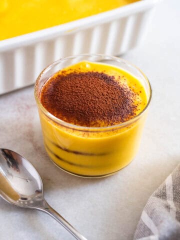 versión individual de la torta en un vaso transparente, mostrando las capas de calabaza y galletas de chocolate, espolvoreada con cacao en polvo.