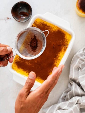 Persona espolvoreando cacao en polvo sobre la tarta utilizando un colador.