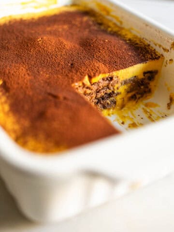 Fuente de tarta de galletas de chocolate con calabaza, con una porción cortada y espolvoreada con cacao en polvo.