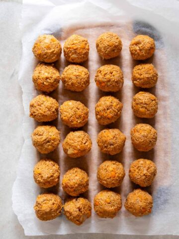 Albóndigas veganas crudas alineadas en una bandeja para enfriar con papel pergamino.