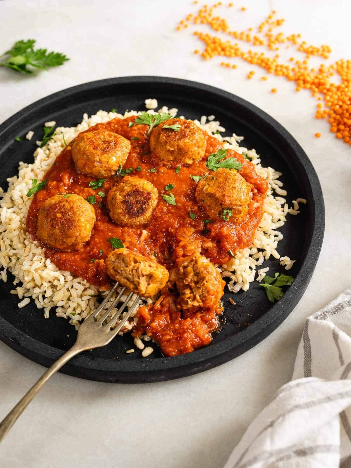 Muestra un plato con albóndigas de lentejas doradas en salsa marinara, servido sobre arroz, decorado con perejil.