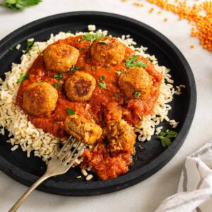 Vista cercana de las albóndigas de lentejas en salsa, servidas sobre arroz.