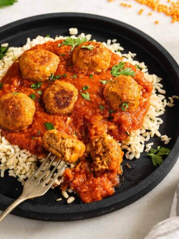 Vista cercana de las albóndigas de lentejas en salsa, servidas sobre arroz.