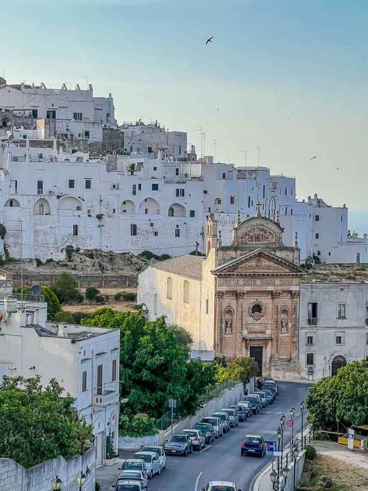 edificios medievales blanco con una catedral en frente con vistas hacia el mar en Ostuni.