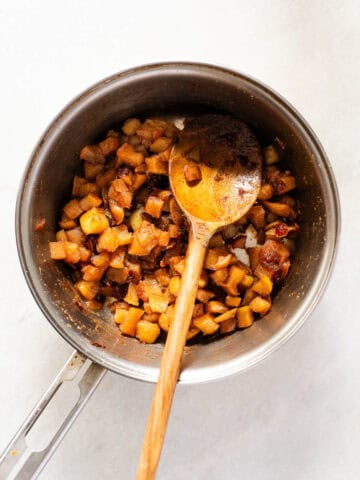 Primer plano de una olla con el relleno de manzana siendo mezclado con una cuchara de madera, mostrando la textura y caramelización de los ingredientes.