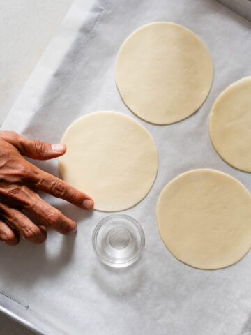 Vista cenital de los discos de empanada colocados en una bandeja de horno con papel encerado, listos para ser rellenados con la mezcla de manzana.