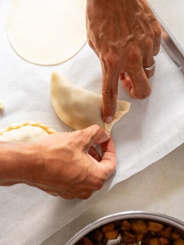 Manos cerrando y sellando una empanada con un tenedor, demostrando el proceso de ensamblaje de la masa.