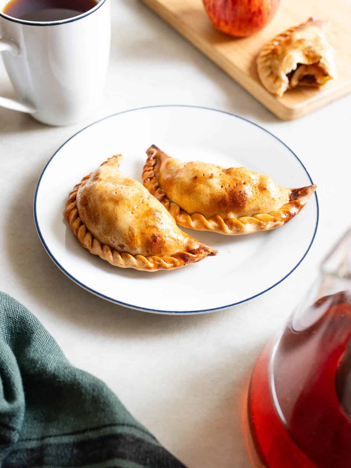 vista de dos empanadas de manzana doradas en un plato blanco con borde azul, destacando su masa hojaldrada.