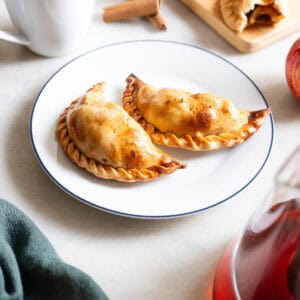 vista de dos empanadas de manzana doradas en un plato blanco con borde azul, destacando su masa hojaldrada.