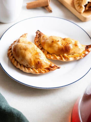 vista de dos empanadas de manzana doradas en un plato blanco con borde azul, destacando su masa hojaldrada.