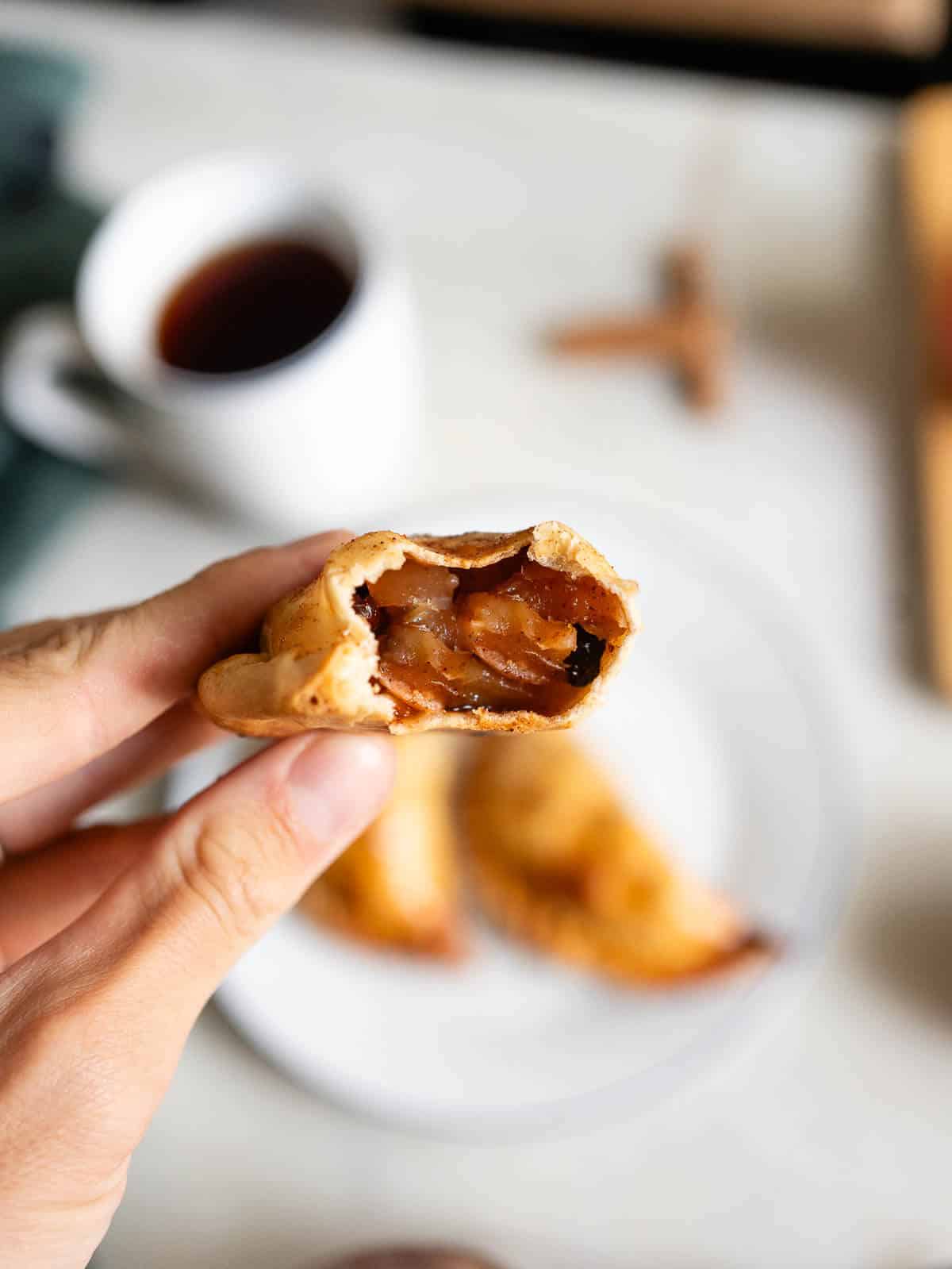 Primer plano de una mano sosteniendo una empanada con un mordisco, revelando el jugoso relleno de manzana en su interior.