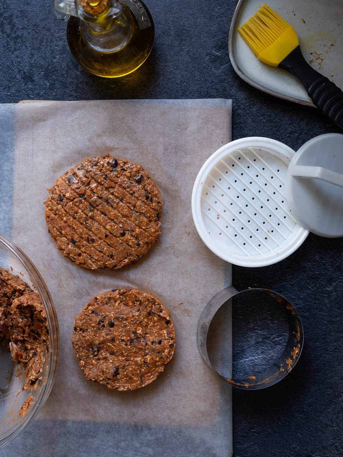 Tres hamburguesas de frijoles negros crudas colocadas sobre una tabla, listas para cocinarse.