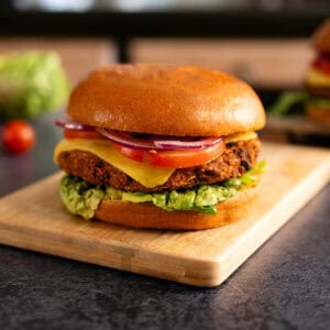 Hamburguesa de frijoles negros servida en un pan con lechuga, tomate, cebolla y queso vegano, vista lateral.