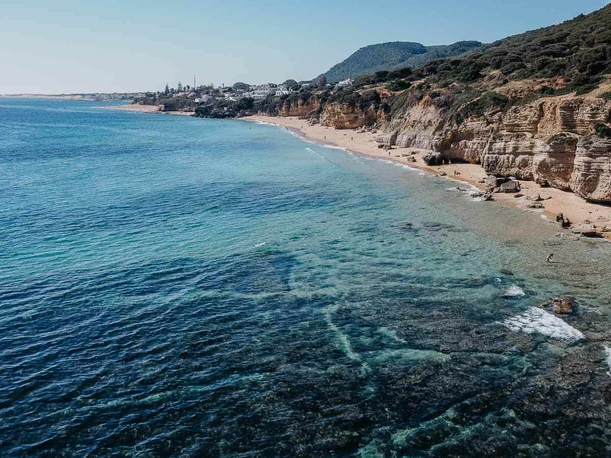 Vista aérea de Caños de Meca, destacando su impresionante entorno natural con dramáticos acantilados y aguas claras y azules.