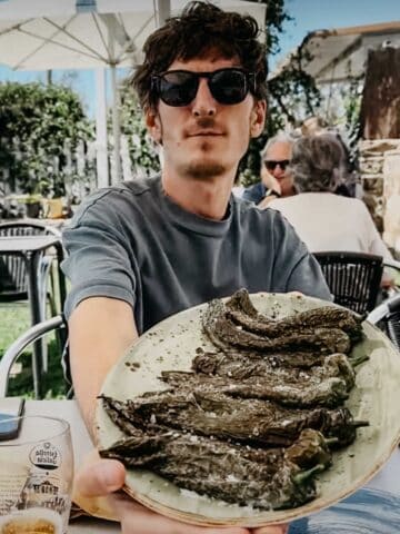 Un hombre sostiene un plato de pimientos verdes asados, sentado al aire libre en el restaurante El Tropezón.